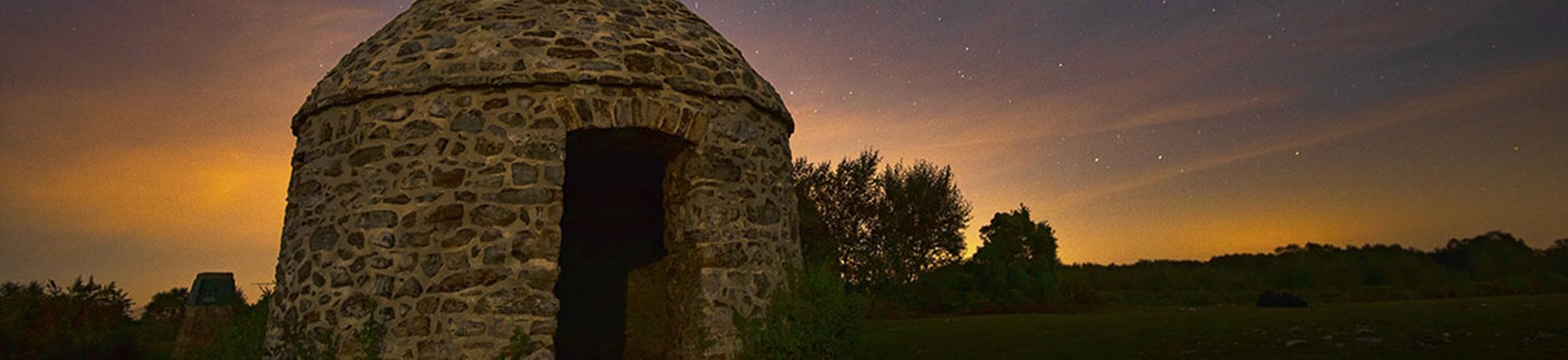 Alt text: A beehive shaped stone building photographed against a starry night sky.