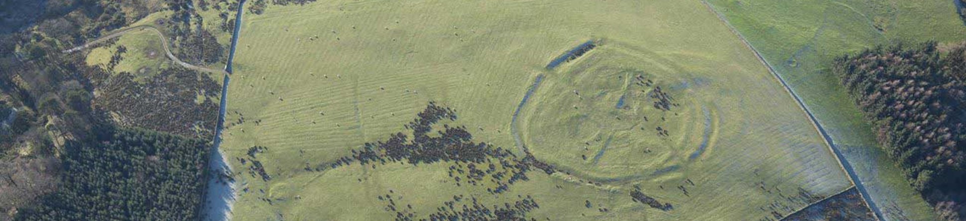 An aerial photograph of a circular enclosure on a hilltop seen as earthworks.
