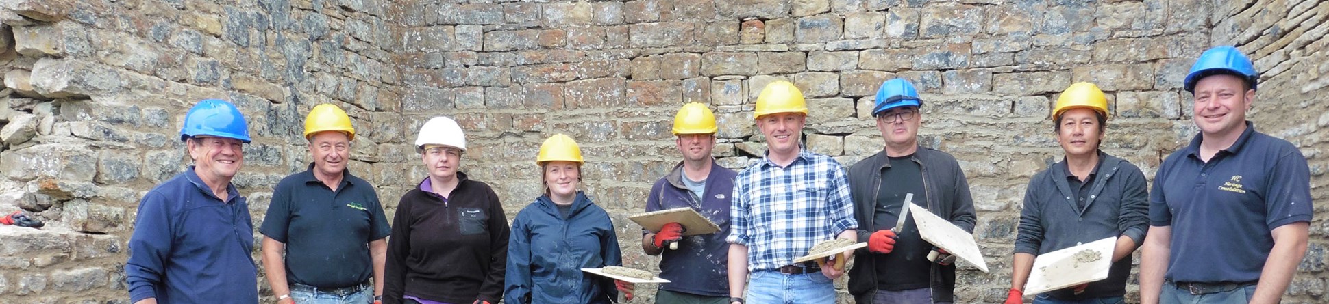  A group of volunteers with repointing tools and buckets of mortar in front of a stone building.