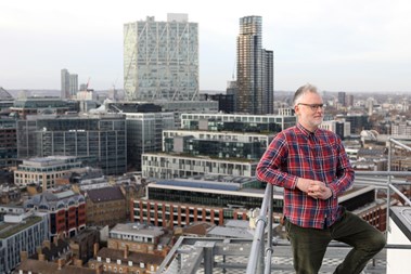 Portrait photo of a man on a roof top with a city skyline behind him. 