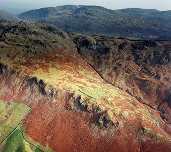 Archive colour aerial photograph showing the outline of a Roman fort on a mountainous promontory.