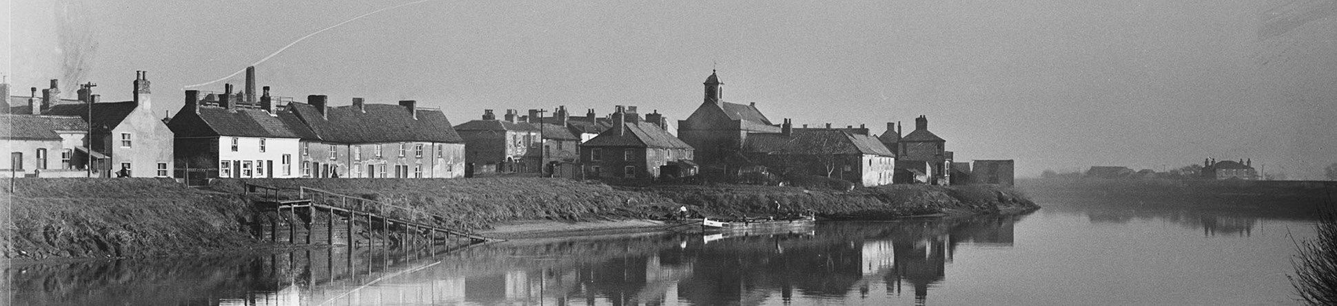 Black and white archive photograph of a townscape viewed across a river.