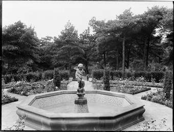 archive black and white photograph of a fountain surmounted by a cherub surrounded by flowerbeds
