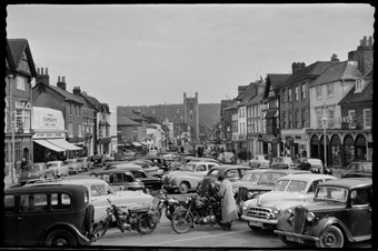archive black and white photograph of a busy street scene with people and vehicles