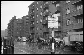 archive black and white photograph of a street scene with parked vehicles