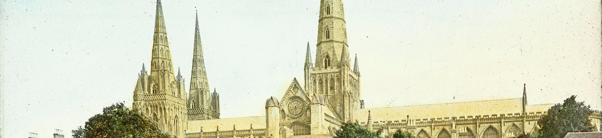 Arcive coloured photo of a Cathedral with a spire behind trees.