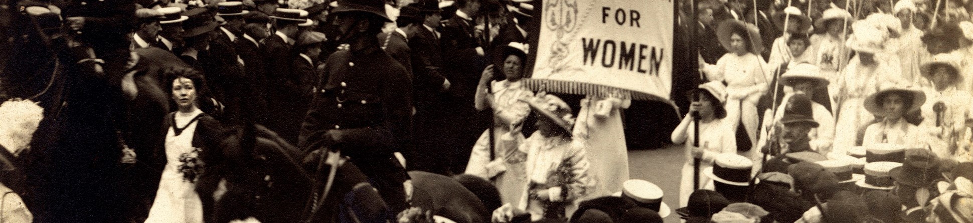 Black and white photo of suffragette procession 1911. Banner text reads: 690 imprisonments to win freedom for women