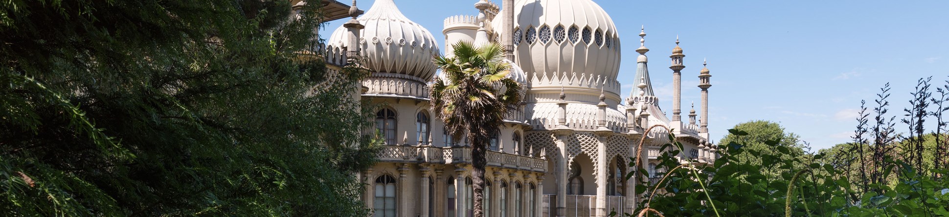 Royal Pavilion Gardens, Brighton, with lush vegetation in the foreground and a clear blue sky behind.