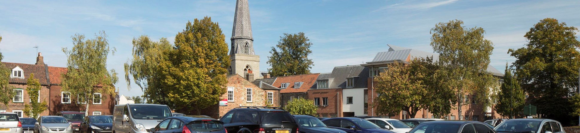 Cars parked in car park with church spire in background