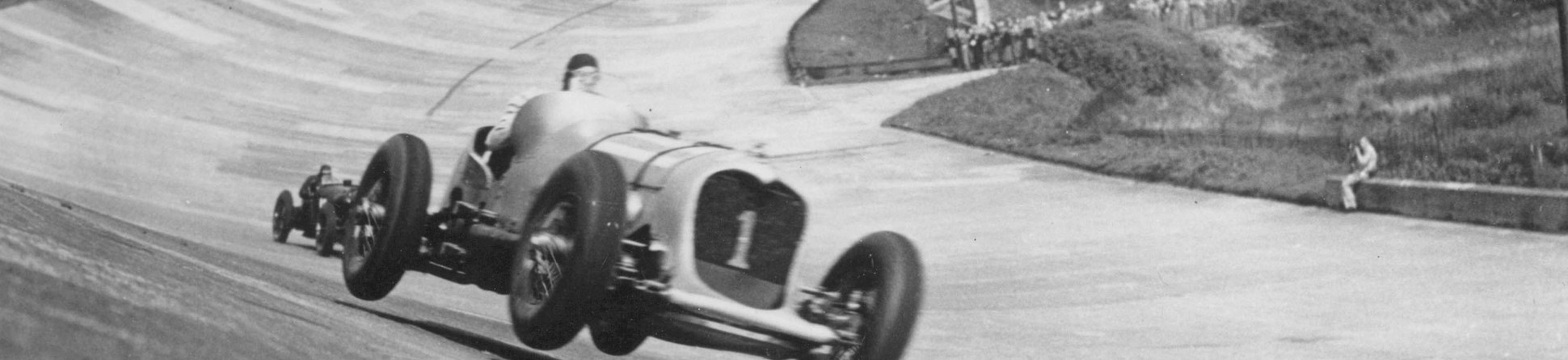 Black and white image of a car lifted off the track at Brooklands as it takes a fast corner.