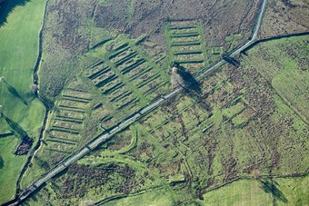 Colour aerial photo showing blocks of low earthwork platforms north of a road with fainter traces of more to the south