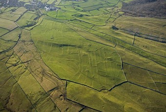 Colour aerial photo showing upland moors divided by dry stone walls with an underlying pattern of regular banks forming fields