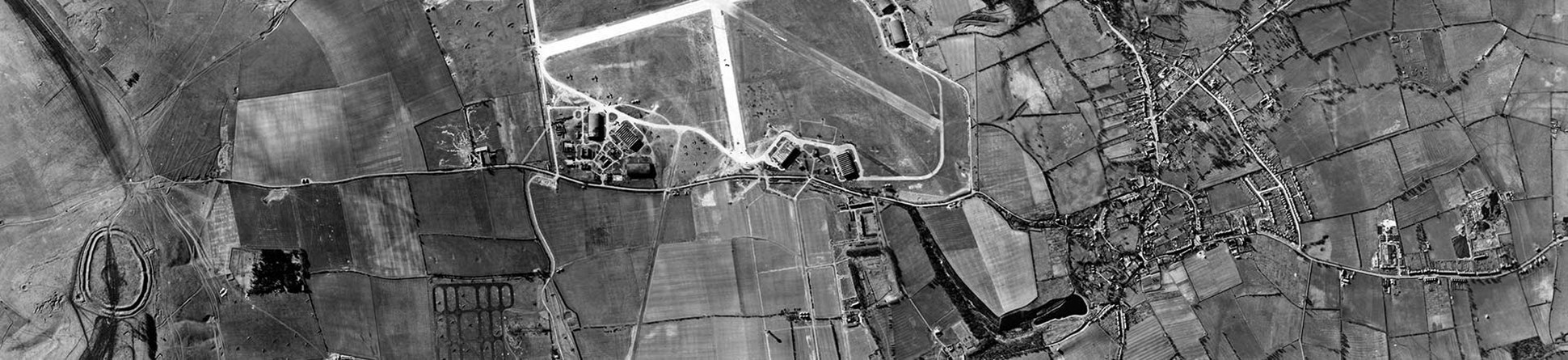 Black and white vertical aerial photograph showing an extensive landscape with fields, roads, houses and an airfield.
