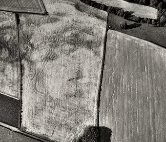 Black and white aerial photo showing arable fields with the outline of the fort seen as dark lines against a pale background