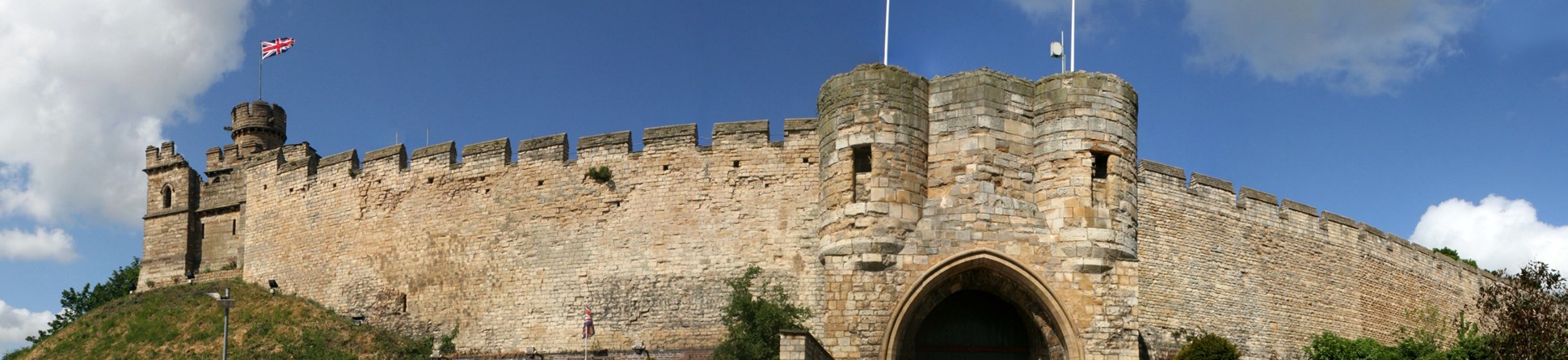 The walls of a large English castle beneath a blue sky with clouds
