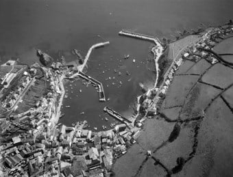 An aerial photograph of a seaside harbour comprising inner and outer harbours with pairs of stone piers. Buildings cluster at the bottom of the photograph.