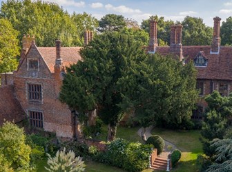 The Elizabethan manor house can be seen from above, surrounded by the garden and trees. A range of chimneys can be seen in the L-shaped building, created of red brick.