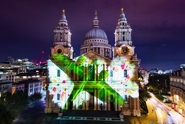 A green bomber plane seen from above is projected across the West elevation of St Paul's cathedral together with architectural plans of the building.
