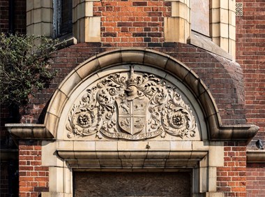 Semi-circular decorative panel above a doorway with coat of arms and foliage.