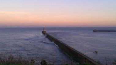 Sun setting in background. Pier, starting in the foreground, running through the middle of the image with lighthouse positioned at the end.