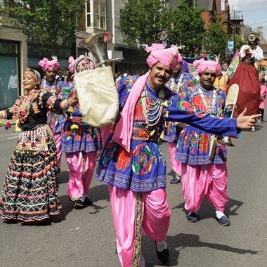 A group of street performers dancing in colourful South Asian-style clothing on a high street.