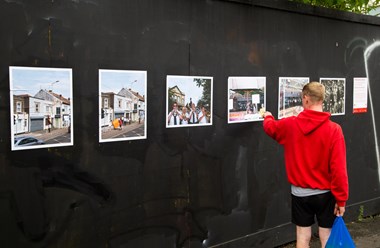 A man carrying a shopping bag stops to look at a photo exhibit.