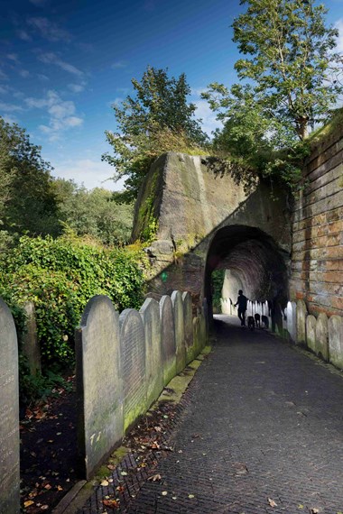 Rock tunnel leading from north of garden to forecourt of Anglican Cathedral with gravestones to the left.