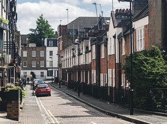 A narrow residential street in London, with brick, tile, and rendered townhouses. 