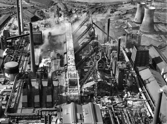A black and white aerial photograph showing an industrial complex with workshops, chimneys and cooling towers.