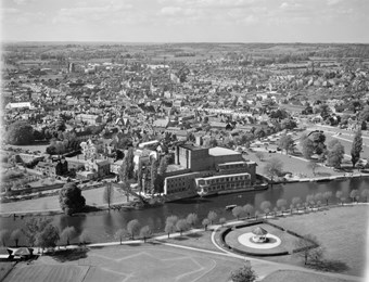 An aerial photograph taken at low altitude. On the far bank of the River Avon stands the Royal Shakespeare Theatre. Stratford town centre extends beyond.