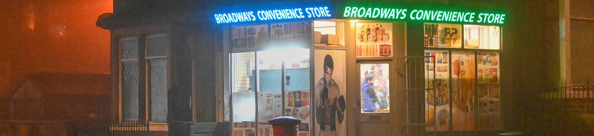 A night time scene showing the illuminated windows of the Broadways Convenience Store.