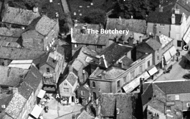 A 1928 black and white image showing a densely packed set of buildings and roofscapes from the air, with alleyways to either side 