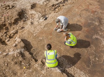 Archaeologists excavating a Roman Mosaic with human figures and a decorative border.