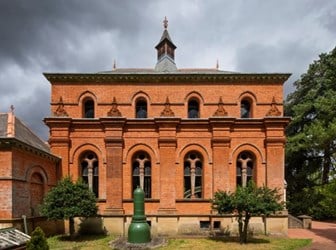 An ornate square red-brick building with short spire, surrounded by trees.