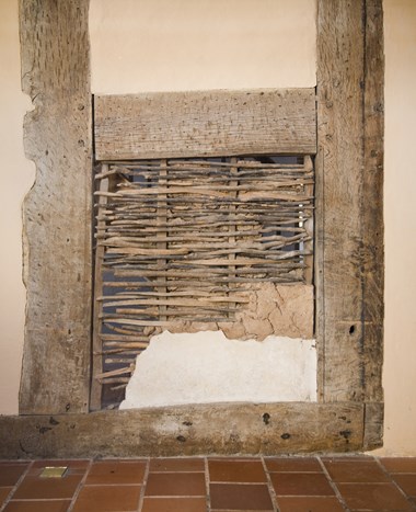 Timbers, rendered panels, and an exposed wattle and daub panel in the interior wall of a farmhouse.