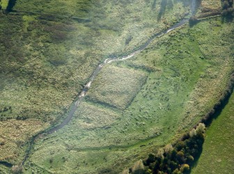 A colour aerial photograph showing earthworks next to a watercourse running through a landscape.