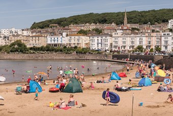 Busy beach with sea wall and Victorian terraces lining the seafront above the beach.