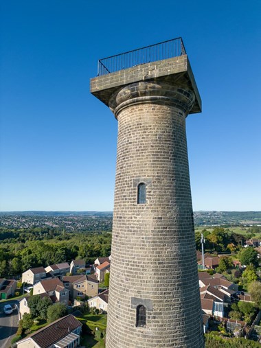 A high angle shot of a large brick-built column, with windows at regular intervals down its height. Houses in the background are dwarfed by its size. 