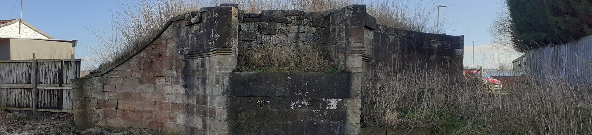 The remains of a stone bridge abutment next to a narrow river. 