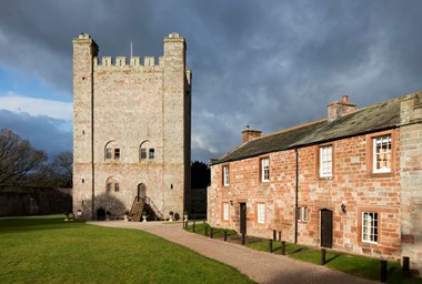 A four-storey stone keep stands alongside stone terraced cottages, in front of a brooding sky.