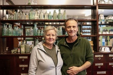 Woman and man standing side by side and smiling in front of shelves with bottles.