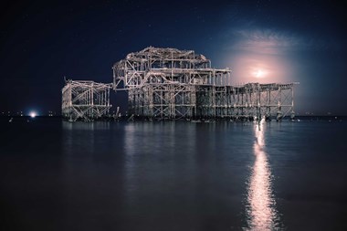 A moonlit photograph of the remains of a large pier structure and water in the foreground.