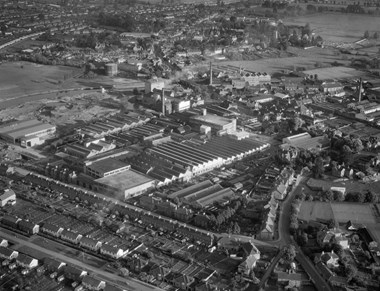 An aerial photograph of a large factory complex surrounded on three sides by streets with terraced and semi-detached housing and industrial buildings.