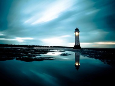 Image taken at sunset, lighthouse appearing to the right. Sea appears in foreground.