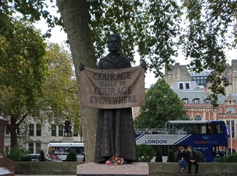 A bronze statue of a woman holding a banner in front of her which reads 'courage calls to courage everywhere'. On the plinth are small portraits of other women.