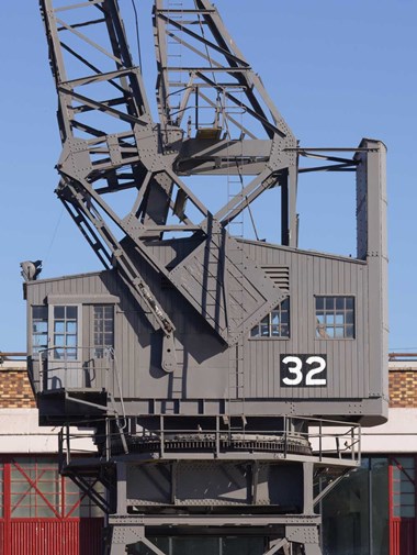 A photograph of the outside of the cab housing the motor room of a large metal crane on a wharfside.