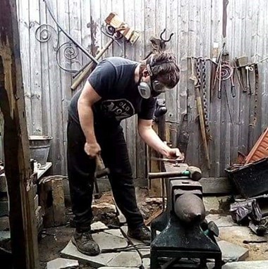 Man wearing a protective mask working metal on an anvil