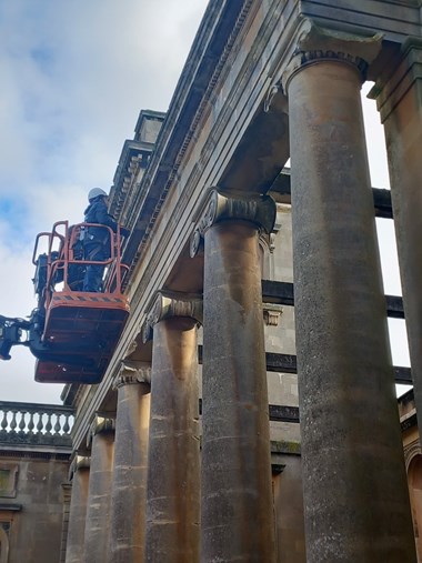 Photograph showing a woman in a hard hat on crane platform working to restore North Portico at Witley Court. 