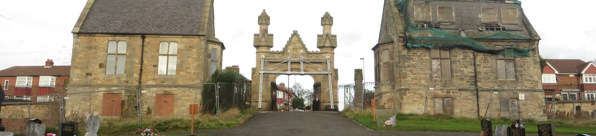 A gate flanked by two buildings in a cemetery. 