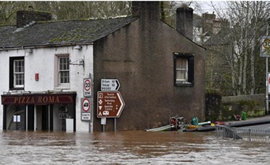 Brown floodwater surrounds a terraced shopfront with a sign saying Pizza Roma.